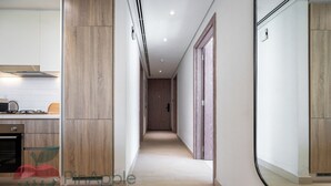A modern kitchen with a built-in stove, a wooden cabinet, and a glass door leading to a hallway. - Spacious 2 Bedroom With Maid Room Near Marina Walk (Dubai)