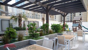 An outdoor patio area with seating and greenery, surrounded by high-rise buildings. - Spacious 2 Bedroom With Maid Room Near Marina Walk (Dubai)