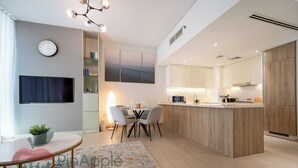 A modern kitchen with wooden cabinets, a built-in island, and a dining area with a table and chairs. - Spacious 2 Bedroom With Maid Room Near Marina Walk (Dubai)