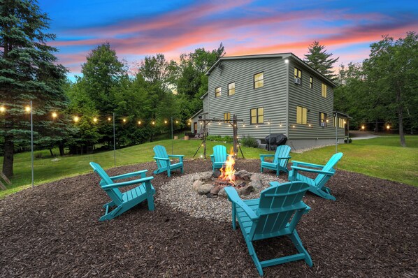 A lodge with a fire pit surrounded by Adirondack chairs, set against a backdrop of a twilight sky.