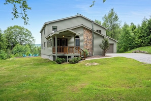 A log cabin with a porch, stone accent wall, and a view of the surrounding forest.