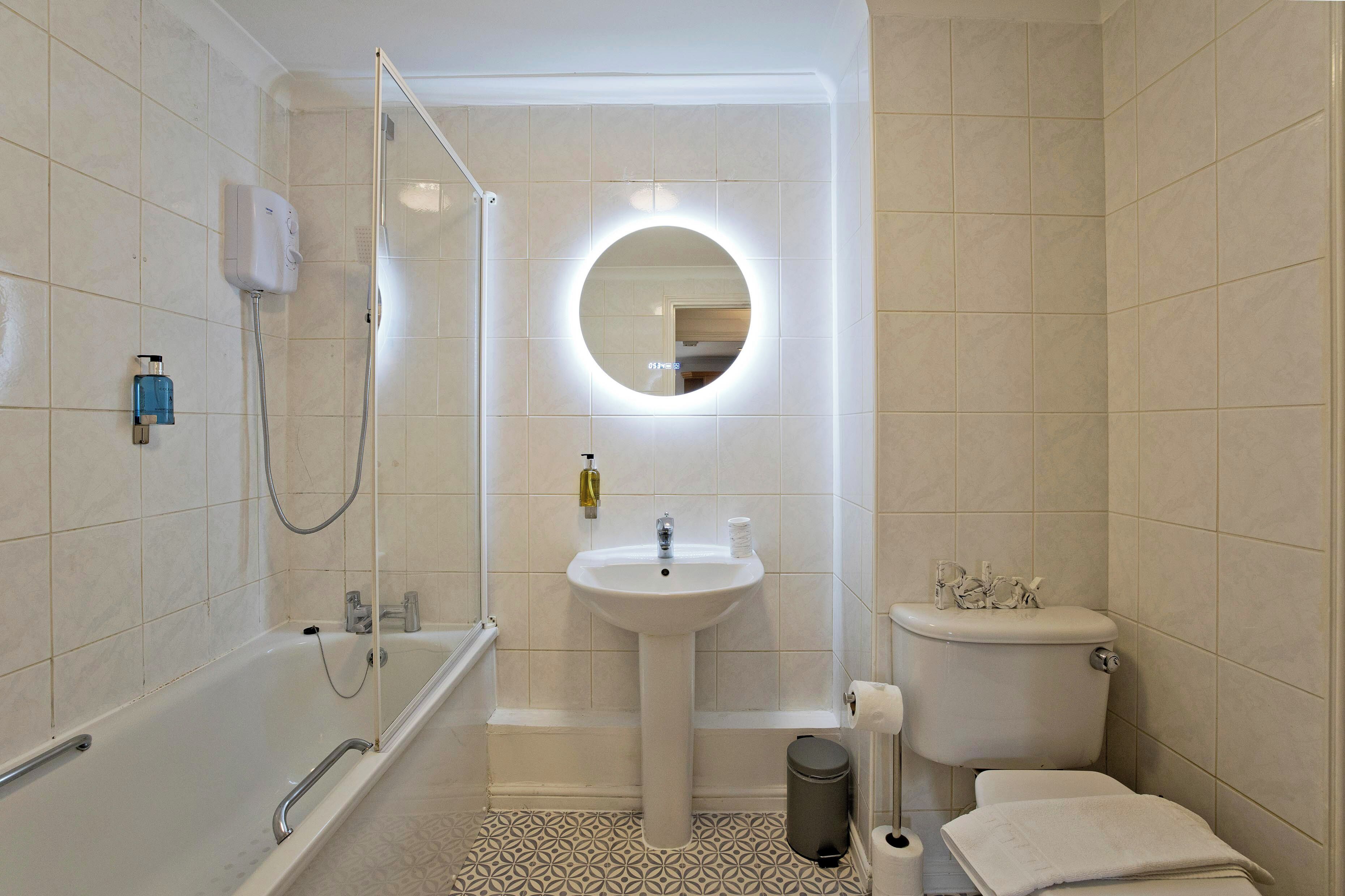 Een badkamer met een badkuip, een wastafel, een toilet en een spiegel met een ronde verlichting.