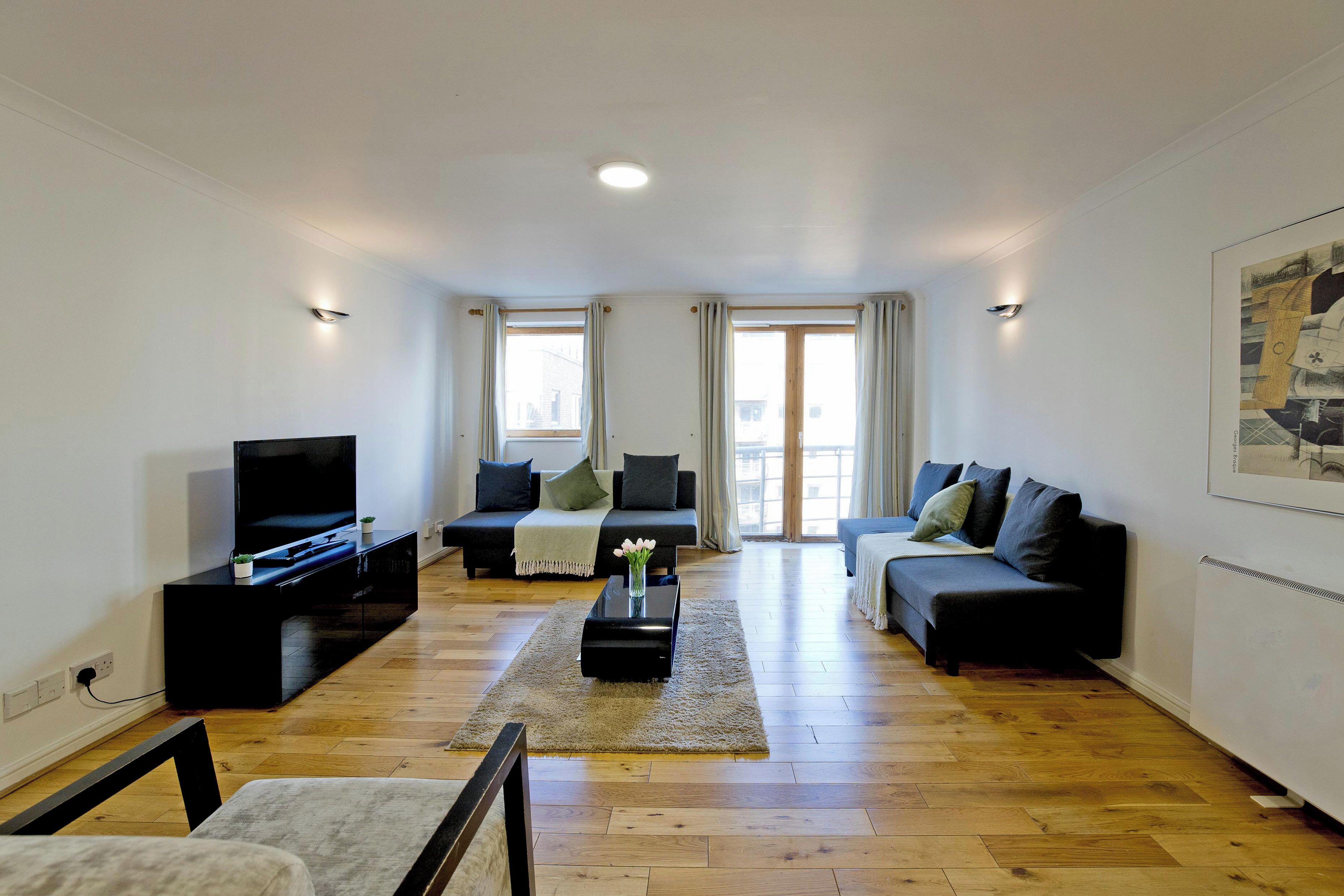 A modern living room with a flat-screen TV, two sofas, a coffee table, and a large window with curtains.