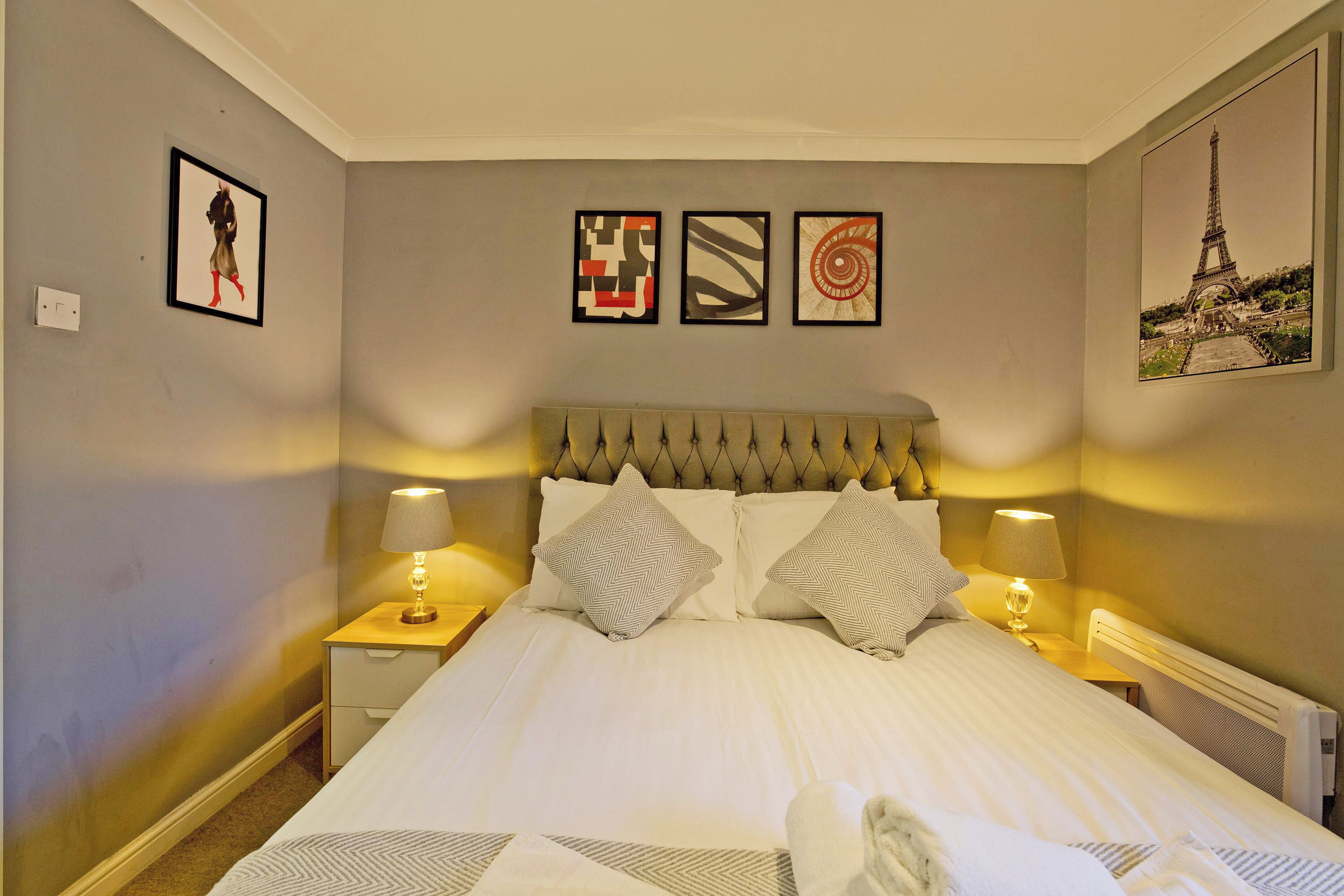 A neatly made bed with a tufted headboard, two bedside lamps, and a framed artwork above the bed.