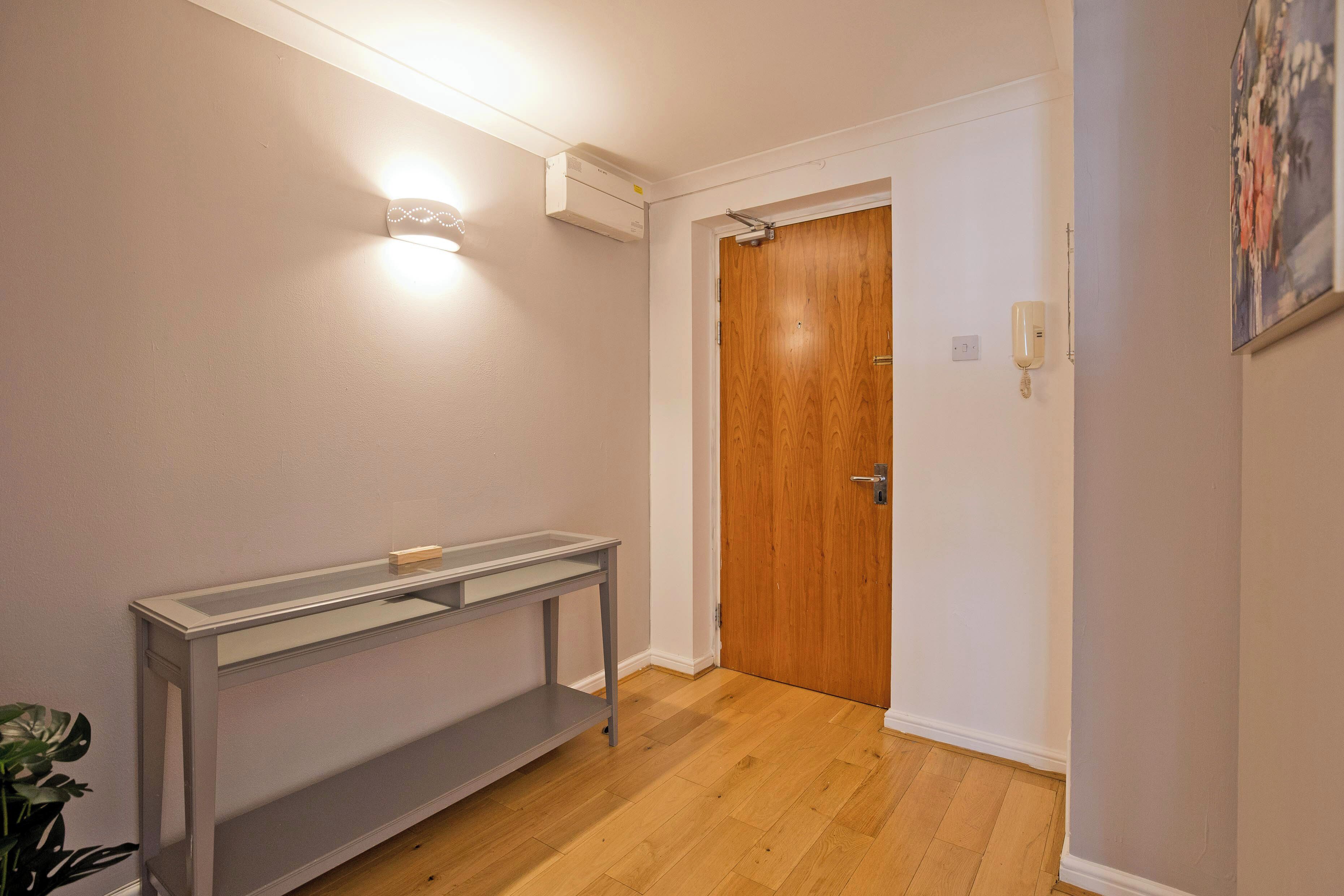 A hallway with a wooden door, a light fixture, and a small table.