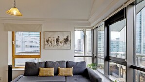 A modern living room with a grey sectional sofa, a small coffee table, and a large window offering a city view. - Imperial Meridian Place Apartment (London)