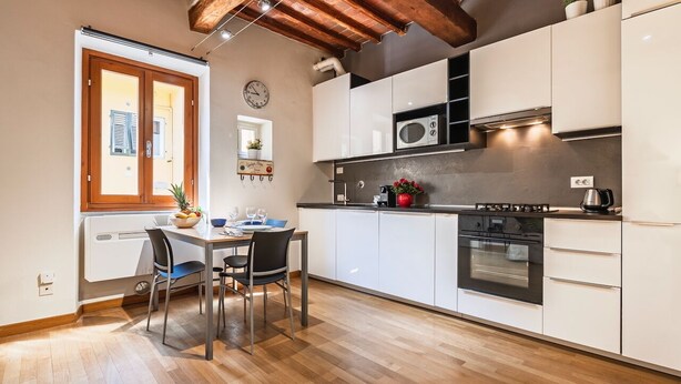 A modern kitchen with white cabinets, a wooden ceiling, and a dining area with a table and chairs. - Porta Romana Charme Flat - Florence Dolce Vita (Florence)