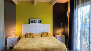 Un dormitorio con una cama, dos mesitas de noche, cabecero y una ventana con cortinas.
