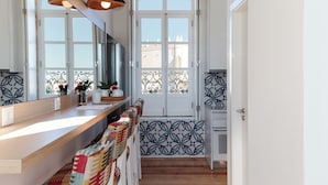 A modern kitchen with a wooden countertop, a large mirror, and a view of the city through a window with decorative iron railings.
