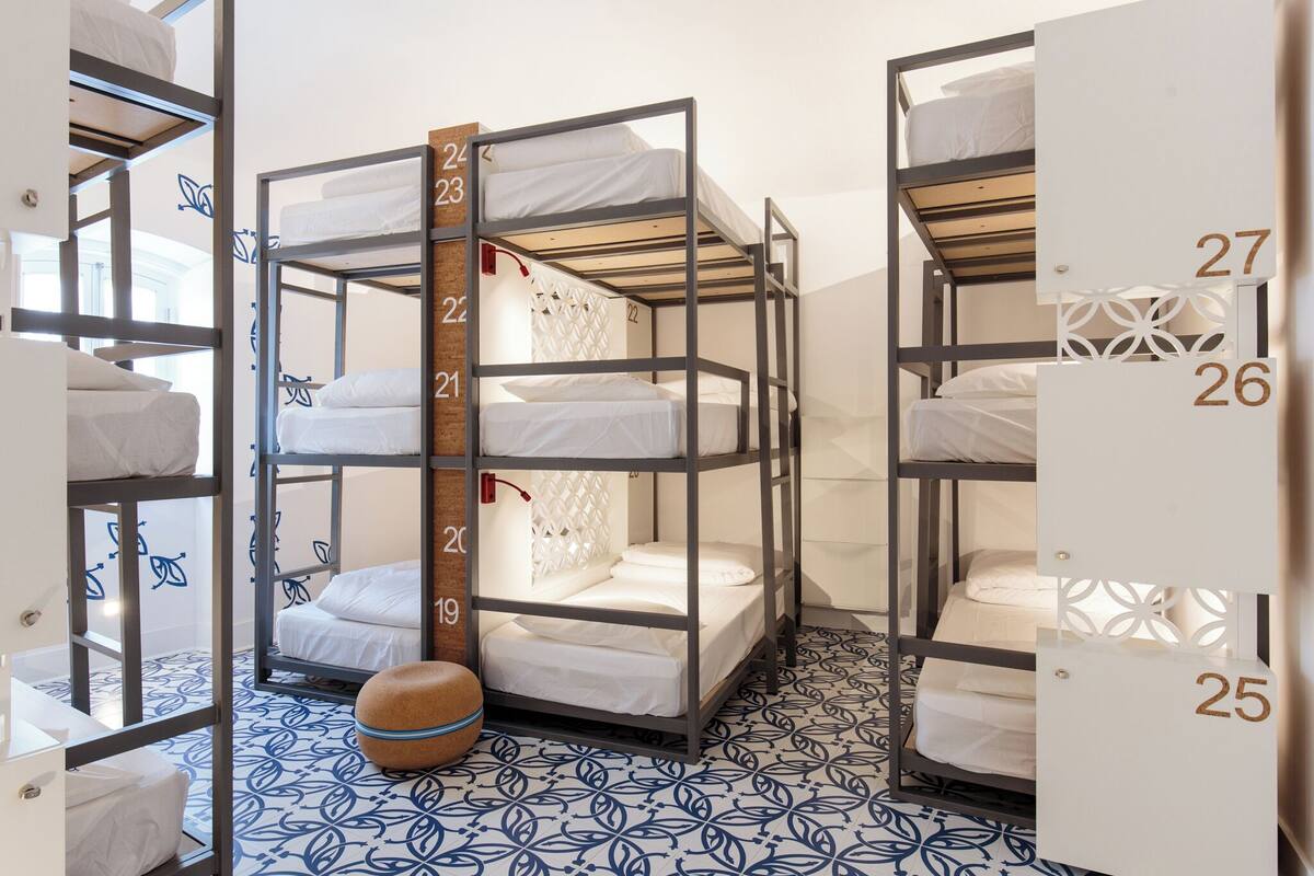 Une chambre de dortoir avec des lits superposés, numérotés de 19 à 27, et un sol à motifs.