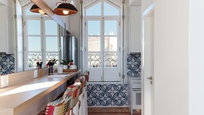A modern kitchen with a wooden countertop, a large mirror, and a view of the city through a window with decorative iron railings. - Heaven Inn Suites & Terrace (Évora)