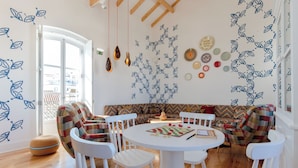A dining area with a round table, white chairs, a patterned sofa, and wall decorations including leaf motifs and plates.
