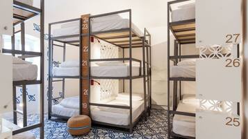 A dormitory room with bunk beds, numbered from 19 to 27, and a patterned floor.
