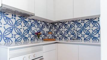 A kitchen with white cabinets, a wooden floor, and blue patterned backsplash.