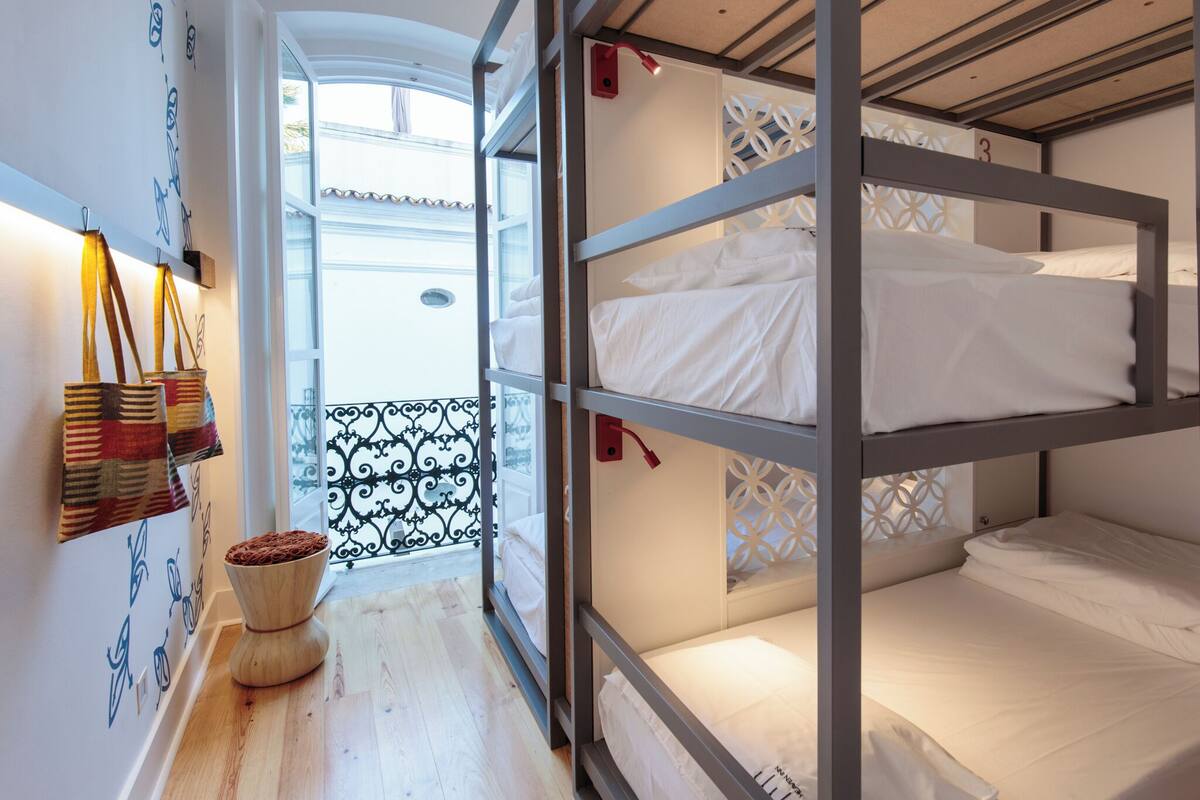 Une chambre avec un lit superposé, un plancher en bois, une petite table sur laquelle se trouve un saladier rempli de fruits, et une vue sur un balcon avec une balustrade.