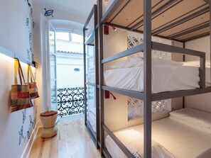 A bunk bed room with a wooden floor, a small table with a bowl of fruit, and a view of a balcony with a railing. - Heaven Inn Suites & Terrace (Évora)