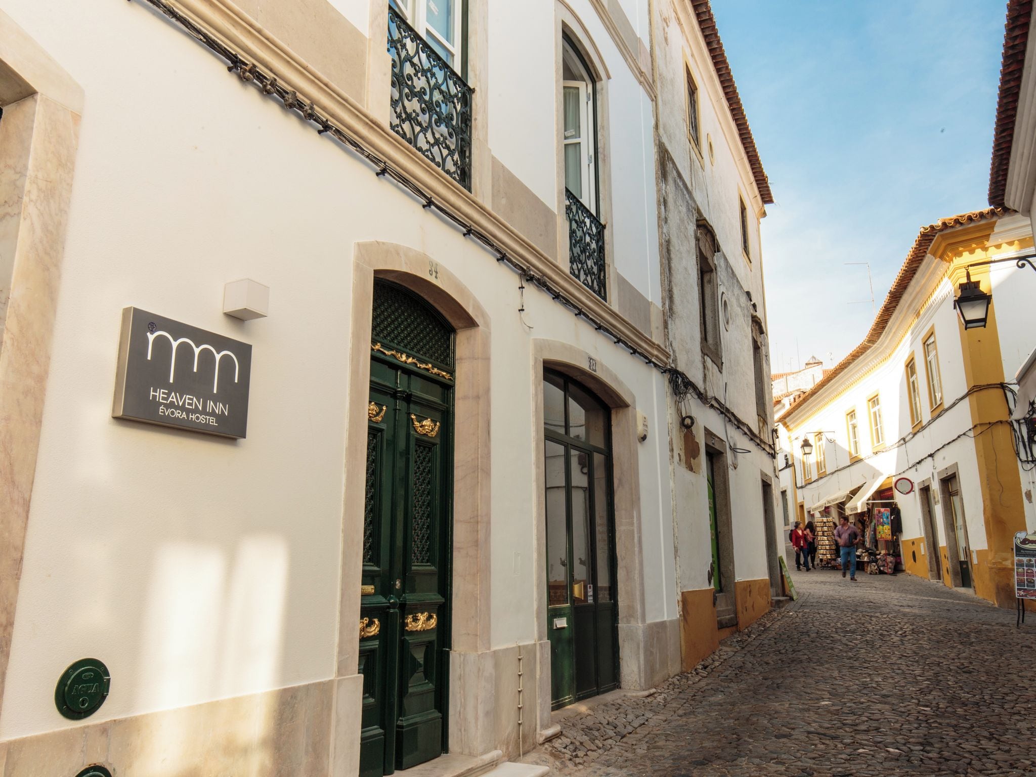 Vista de calle con un edificio que dice 'Heaven Inn Évora Hostel', con una calle empedrada, arquitectura tradicional y cielo despejado.