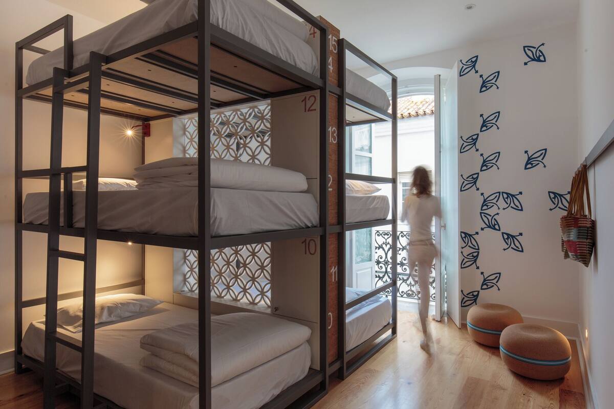 Une chambre avec des lits superposés, chaque lit étant identifié par un numéro, un mur décoré de motifs et une fenêtre offrant une vue.