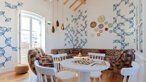 A dining area with a round table, white chairs, a patterned sofa, and wall decorations including leaf motifs and plates. - Heaven Inn Suites & Terrace (Évora)