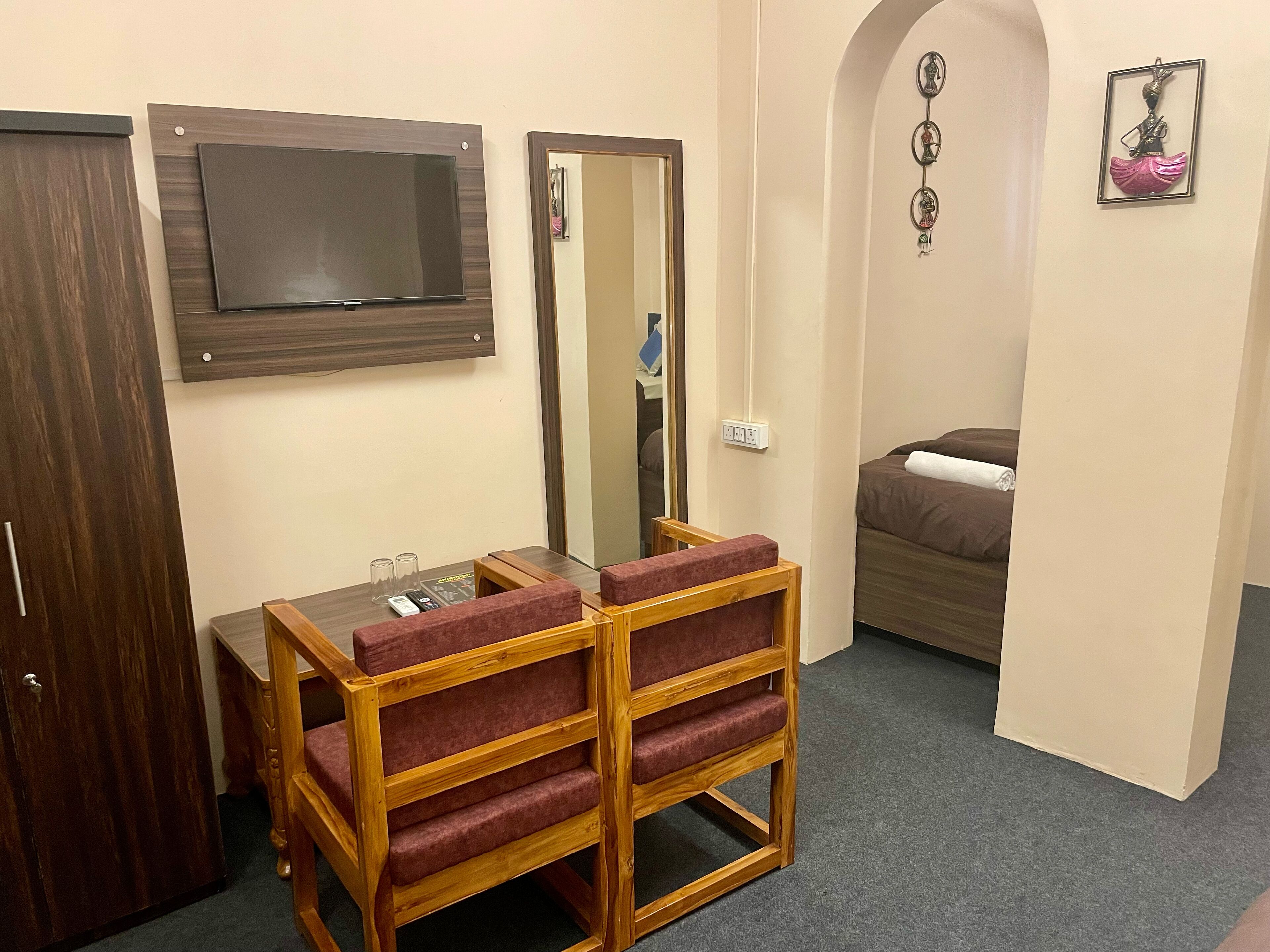 A compact room with a wooden desk, a mirror, a bed, and a small seating area.