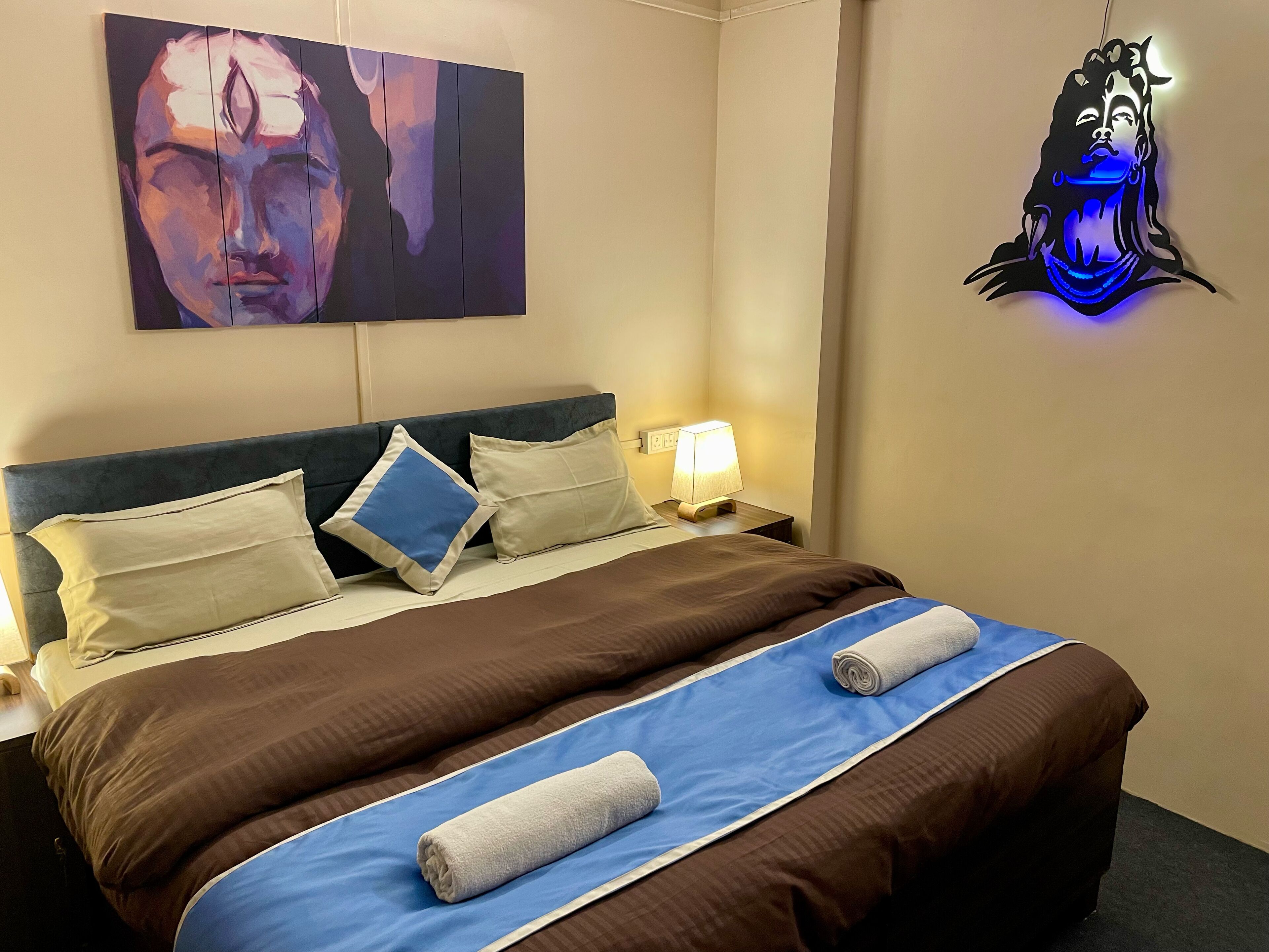 Una camera d'albergo con un letto, cuscini, una lampada da comodino e un quadro appeso al muro.