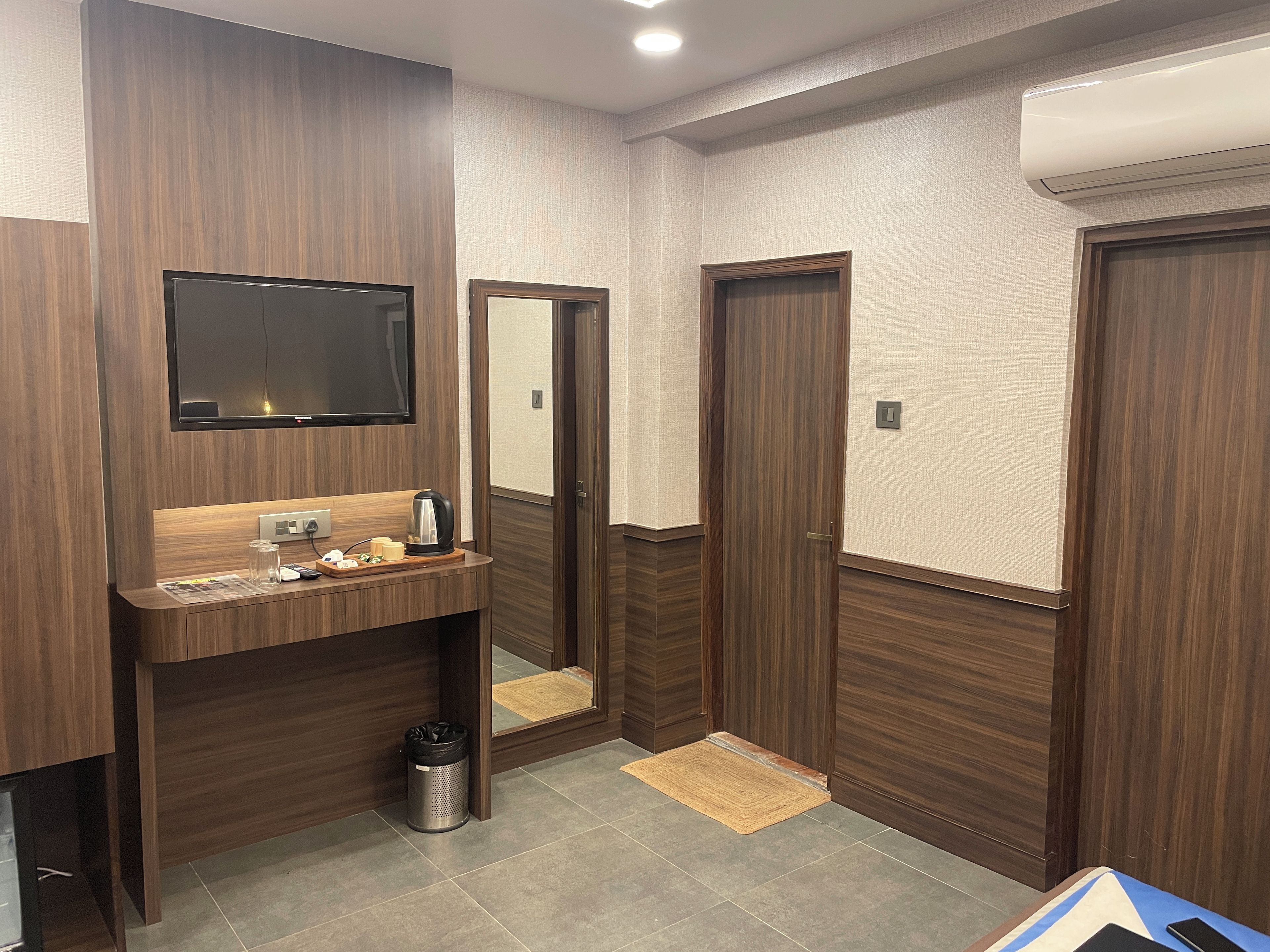 A modern bathroom with a wooden vanity, a mirror, a television, and a trash bin.