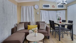 Una sala de estar con sofá, una mesa de centro y una mesa de comedor con sillas. Hay un reloj en la pared y un adorno sobre la mesa de comedor.