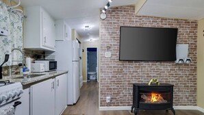Una cocina moderna con armarios blancos, un microondas y una estufa a gas. Hay una chimenea con un televisor montado encima.