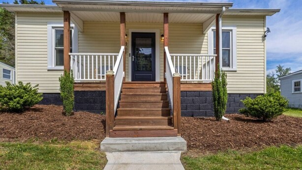 Ein eingeschossiges Haus mit einer Veranda, einer Holztreppe und einer schwarzen Tür.