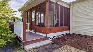 Eine überdachte Veranda mit Holzdeck, weißer Geländer und einem Bereich mit Fliegengittern.