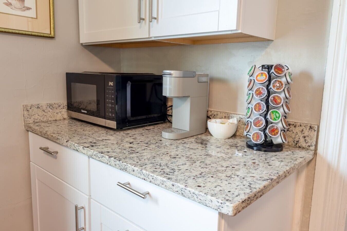 Una cocina equipada con microondas, cafetera y soporte para cápsulas de café.