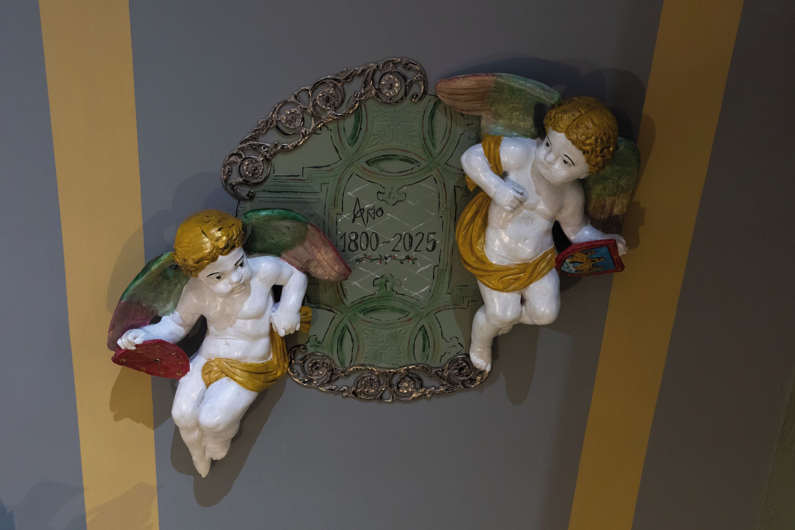 Una placa decorativa con querubines y un rango de fechas de 1800 a 2025.