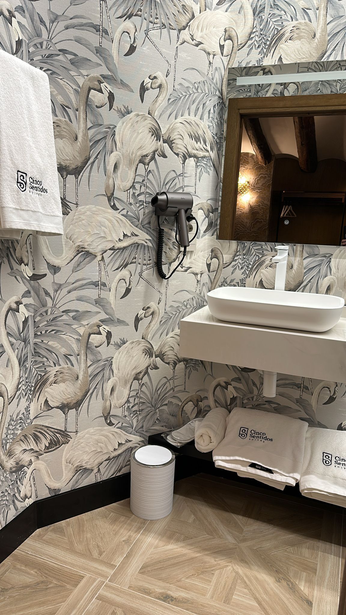 Un baño con papel tapiz floral, un lavamanos blanco, un toallero y un secador de pelo.
