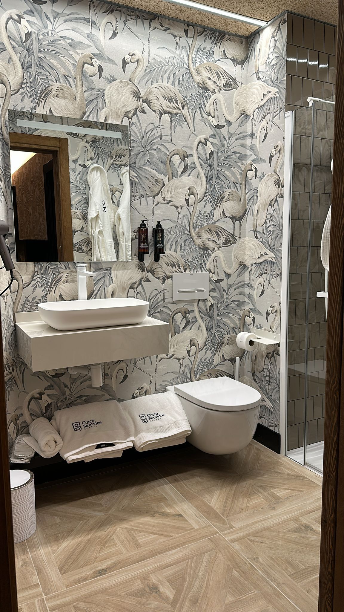Un baño con lavamanos, espejo y retrete, decorado con un estampado floral.