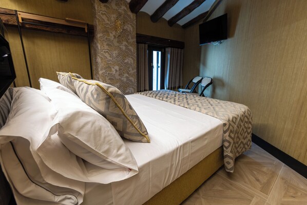 A neatly made bed with patterned bedding, a wooden headboard, a television mounted on the wall, and a window with curtains. - 5 Sentidos - Suites de Lujo (Tudela)