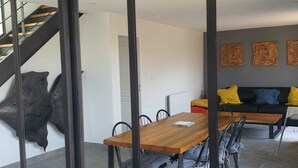 A modern dining area with a wooden table and chairs, a staircase, and a living area with a sofa and cushions.