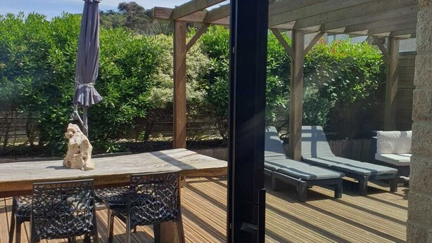 An outdoor patio with a wooden table and chairs, a stone sculpture, and a pergola with lounge chairs.
