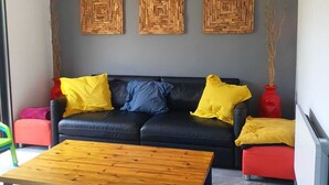 A modern living room with a black leather sofa, yellow and blue cushions, a wooden coffee table, and three woven wall art pieces.