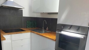 A modern kitchen with white cabinets, a stainless steel oven, a wooden countertop, and a green backsplash.