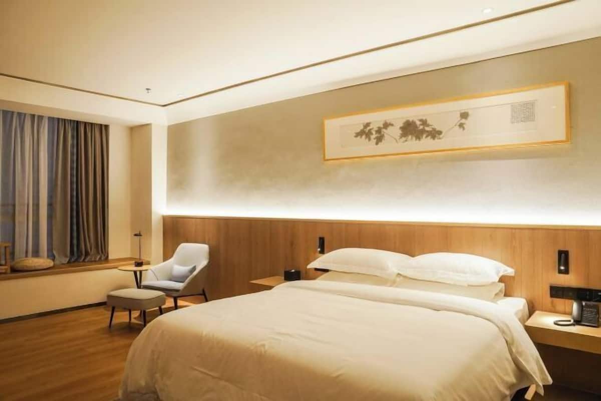 A hotel room with a large bed, a chair, a bedside table, and a wall-mounted artwork.