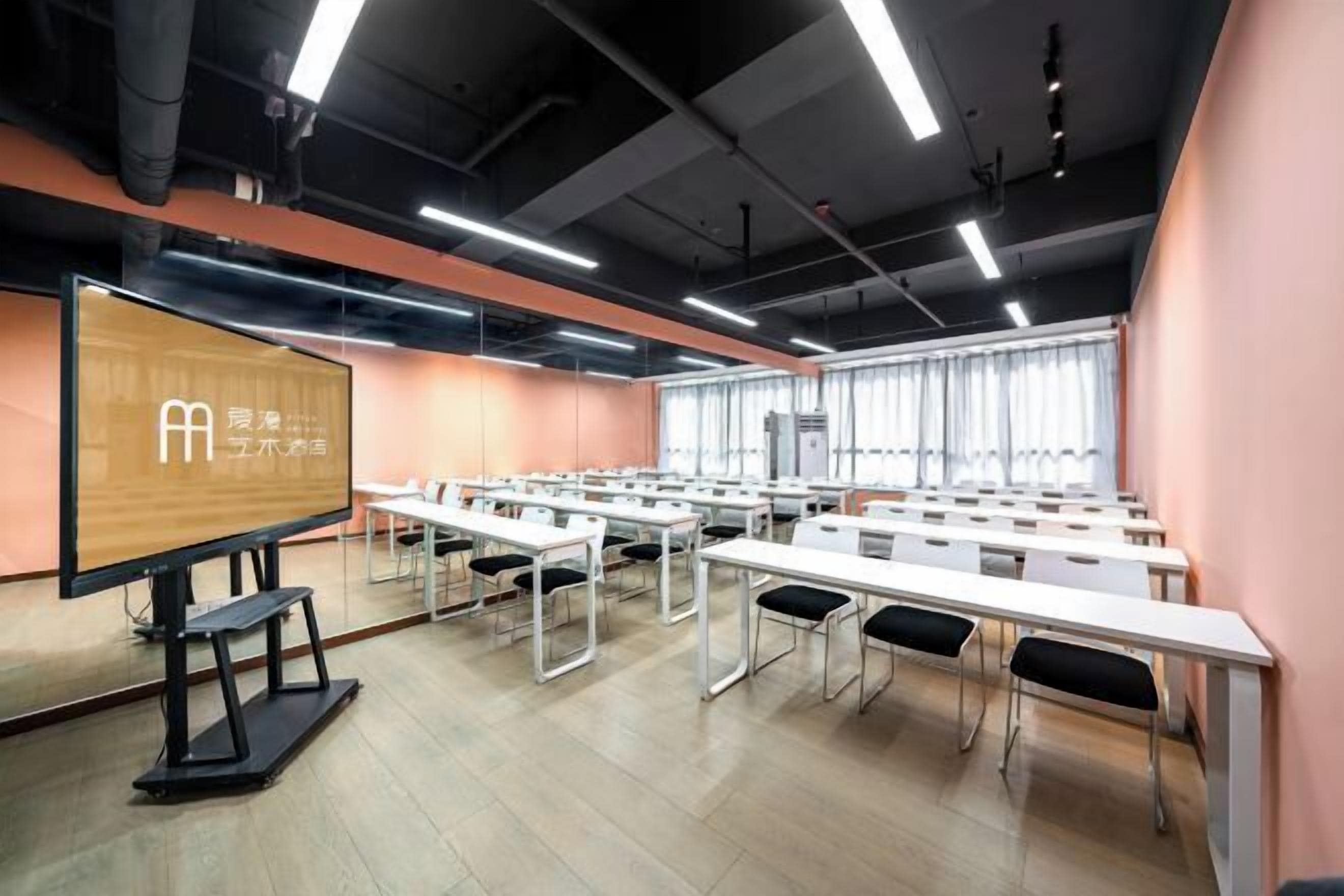 A conference room with white tables and chairs, a large screen, and a wooden panel with text.