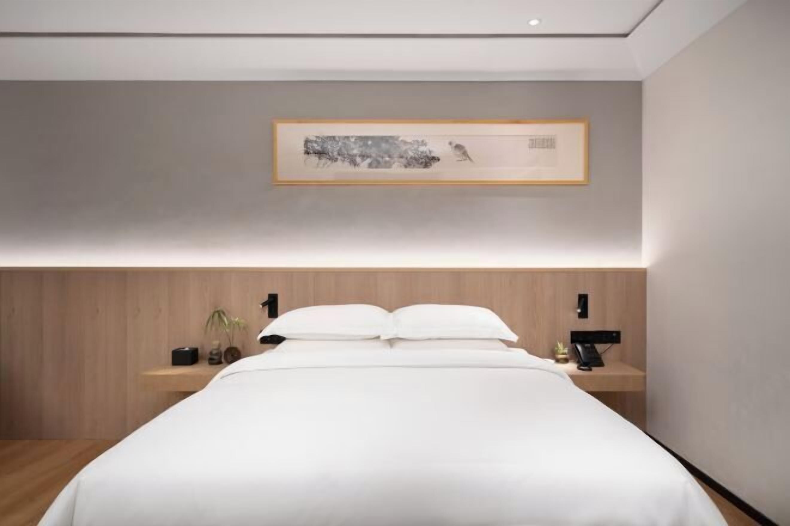 A modern bedroom with a large bed, bedside tables, a wall-mounted artwork, and a wooden headboard.