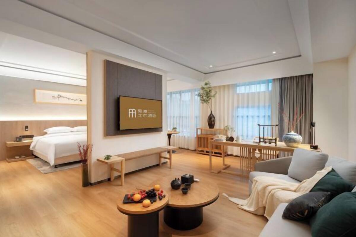 A modern hotel room with a bed, a desk, a sofa, and a dining area.