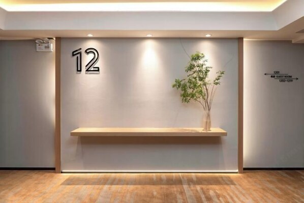 Un comptoir d’accueil avec une plaque portant le numéro « 12 », un panneau indiquant la direction des chambres, et une plante sur le comptoir.