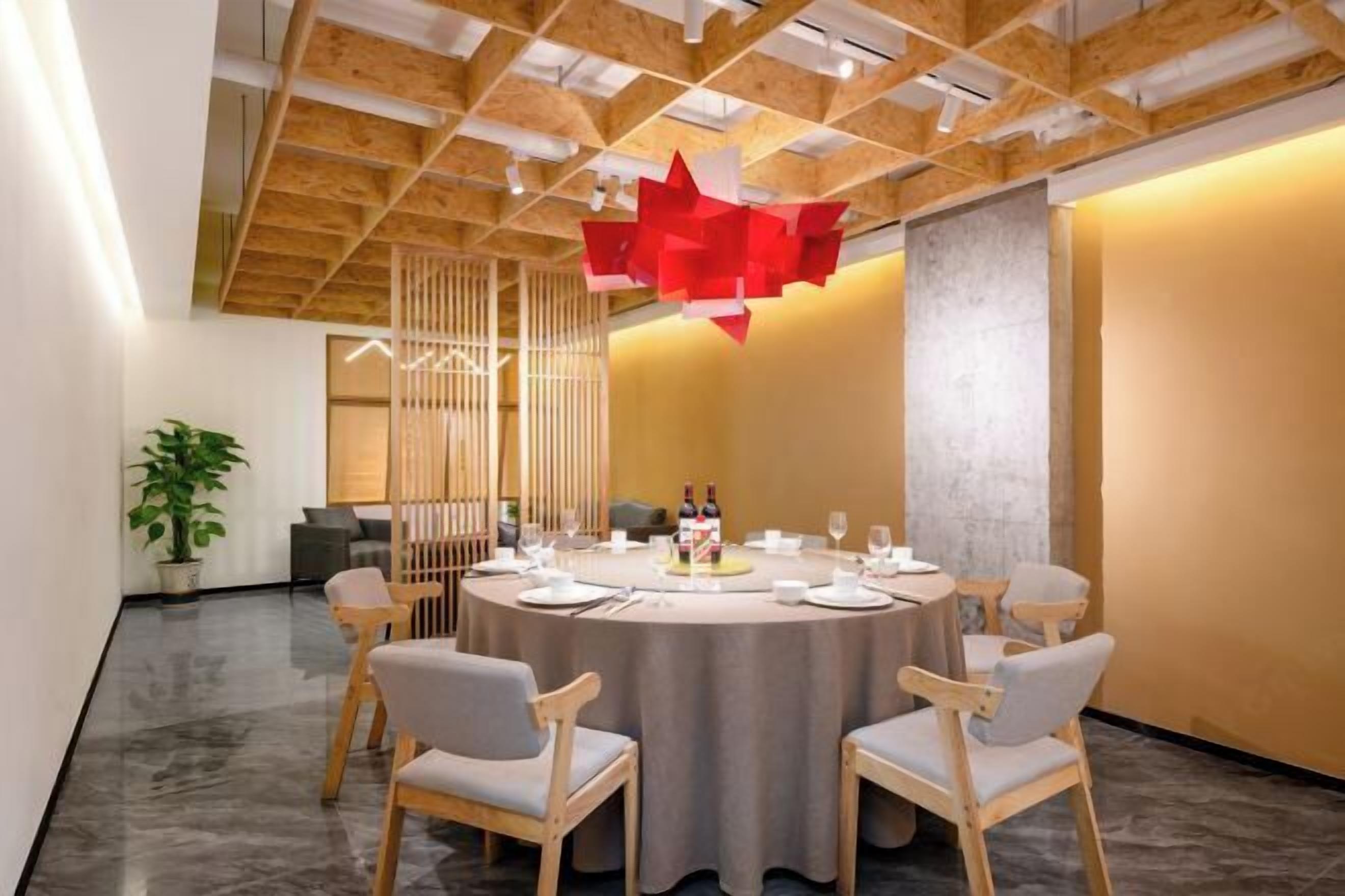 Un salón de conferencias moderno con una mesa redonda, sillas de madera y una lámpara abstracta roja.