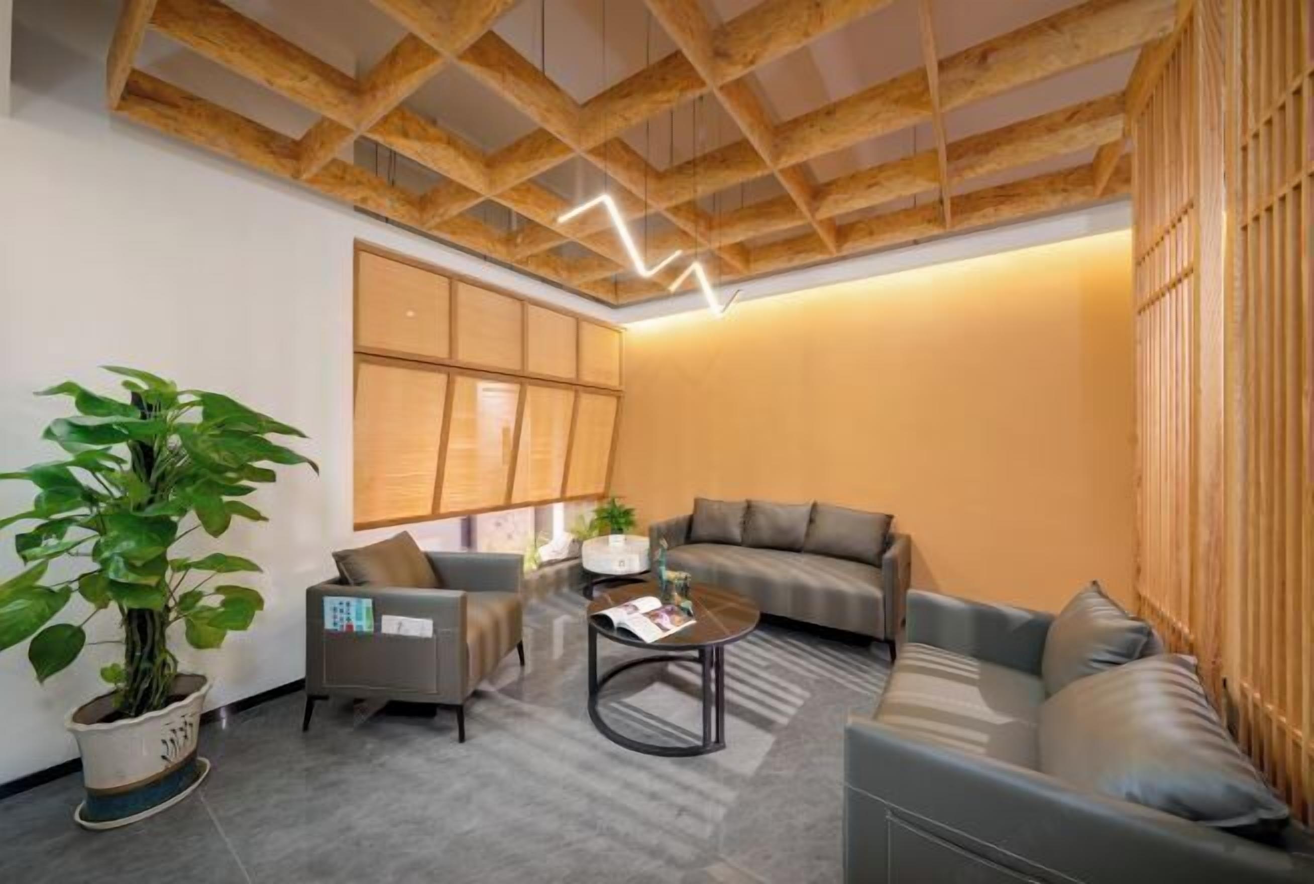 Una sala de estar moderna con techo de madera, sofás grises, una mesa de centro y una planta grande en maceta.