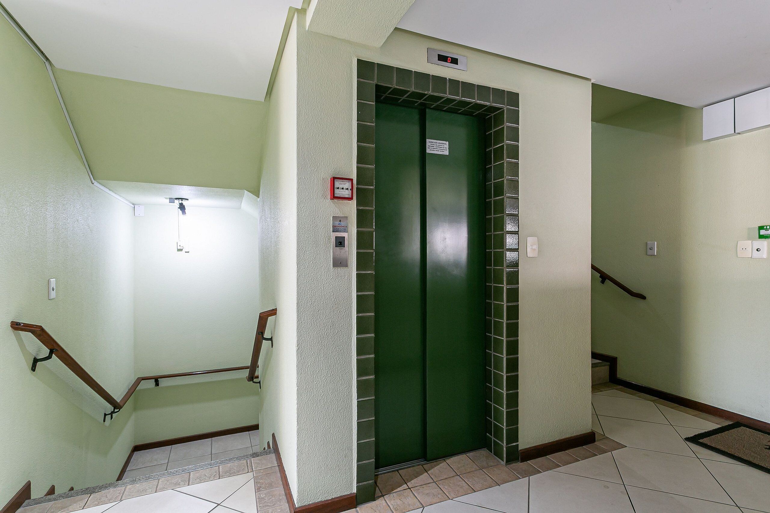 A green elevator with a digital display, a handrail, and a sign on the wall.