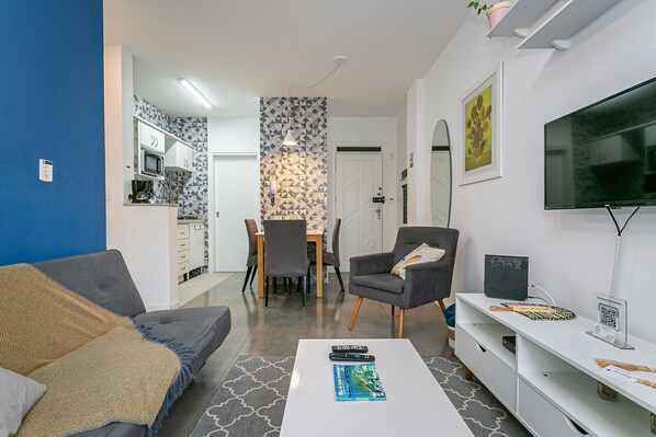 A modern living room with a sofa, coffee table, TV, and a dining area with chairs and a table.