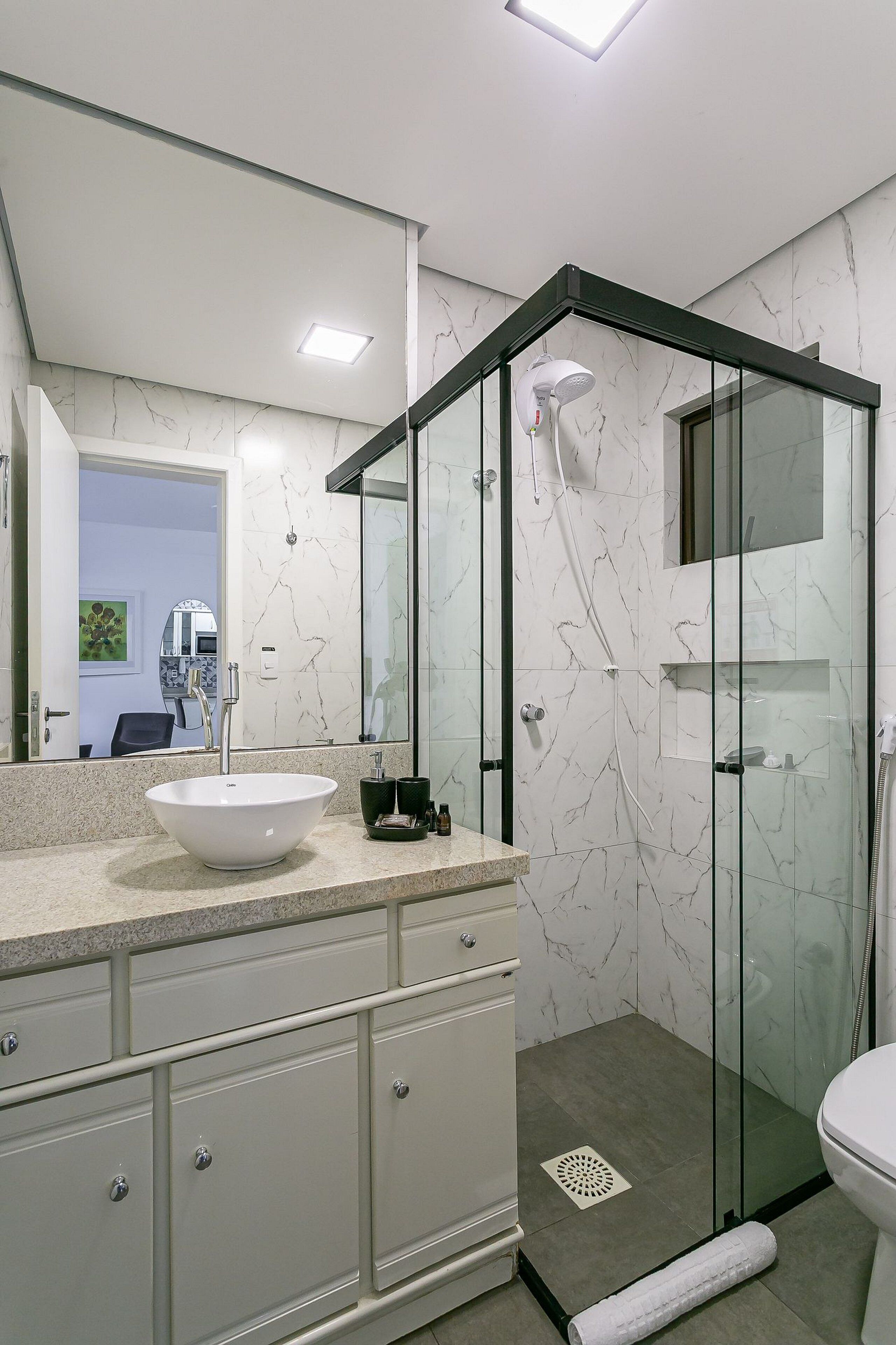 Une salle de bain moderne avec une douche à parois de verre, un lavabo blanc et un pare-baigneoire en marbre.