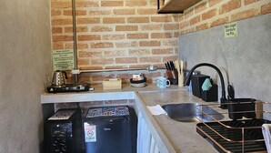A compact kitchen with a brick wall, wooden ceiling, and a tiled floor.